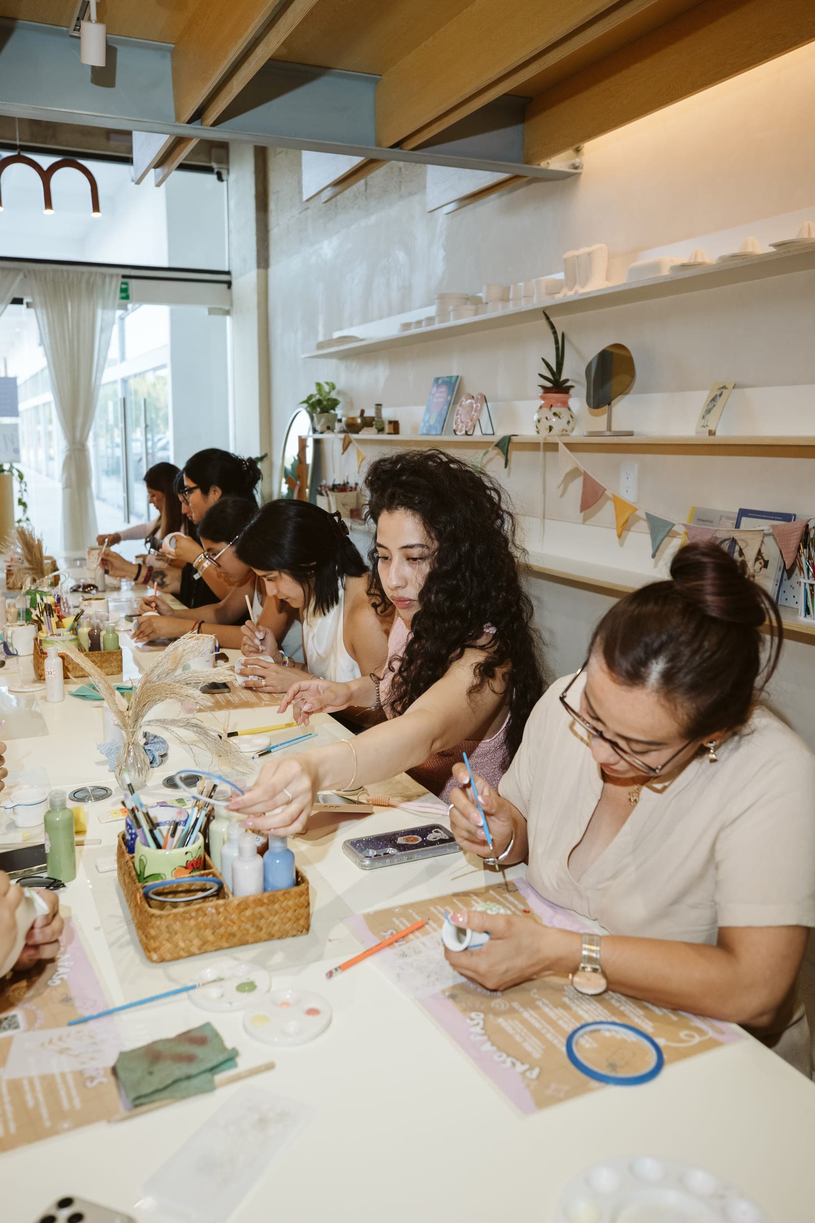 Varias personas pintando cerámica juntas alrededor de la mesa larga del taller